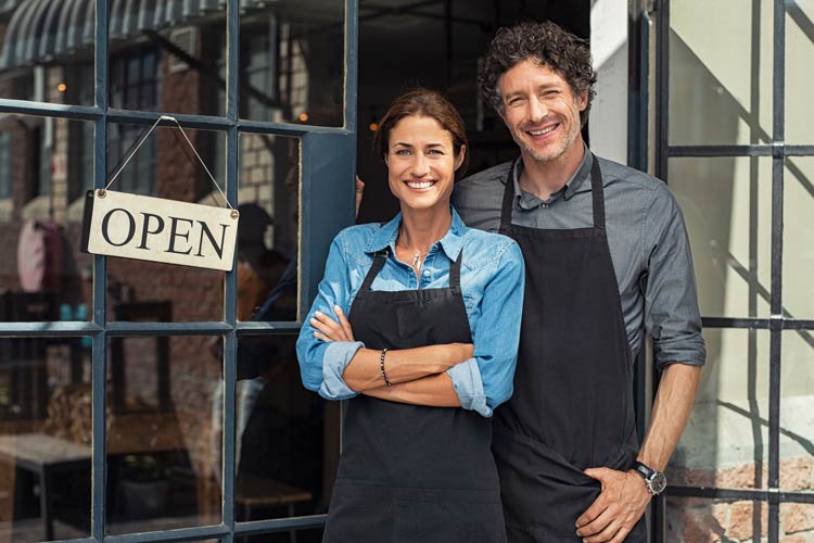 small business owners stand in front of their shop smiling